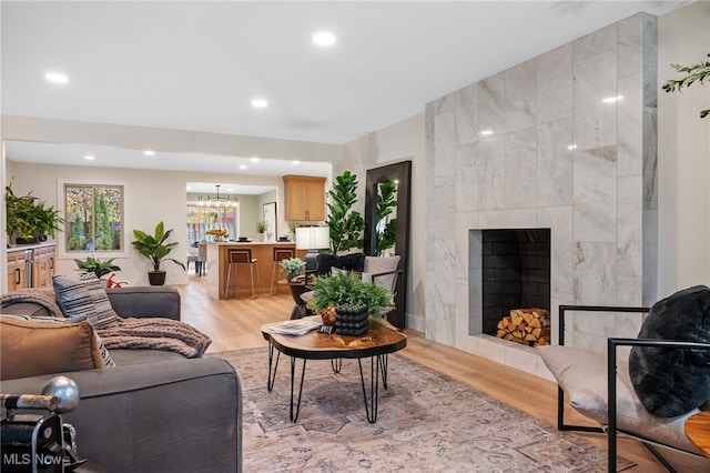 living room with a tiled fireplace, an inviting chandelier, and light hardwood / wood-style flooring