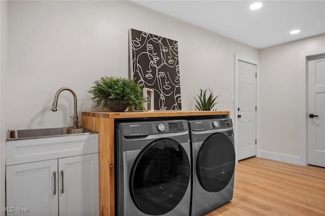 clothes washing area with washing machine and clothes dryer and light wood-type flooring