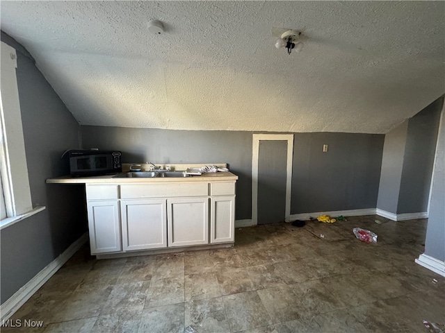 interior space with sink, white cabinetry, lofted ceiling, and a textured ceiling