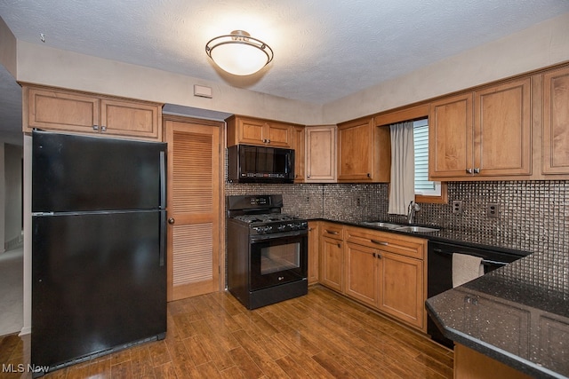 kitchen with dark wood-type flooring, black appliances, sink, decorative backsplash, and dark stone countertops