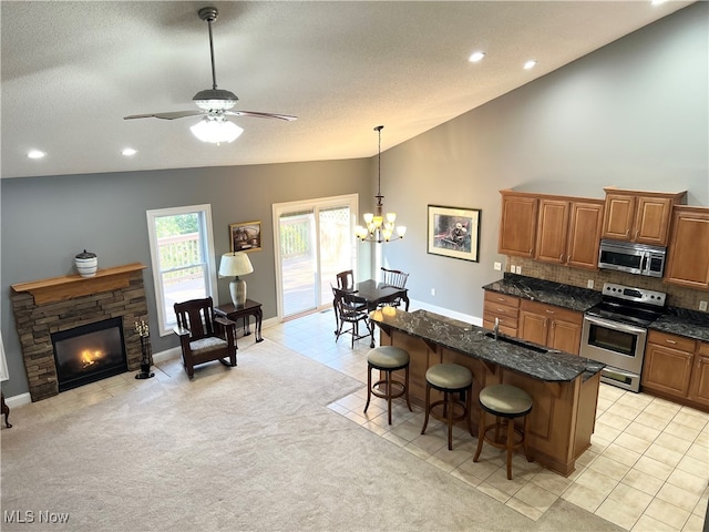 kitchen with a center island with sink, light colored carpet, a fireplace, appliances with stainless steel finishes, and a kitchen bar