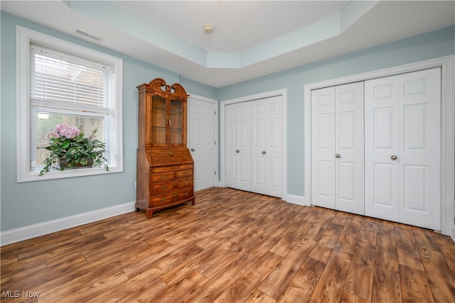 unfurnished bedroom featuring hardwood / wood-style floors, two closets, and a raised ceiling