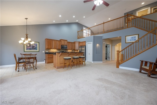 kitchen featuring light carpet, high vaulted ceiling, ceiling fan with notable chandelier, decorative backsplash, and a kitchen bar