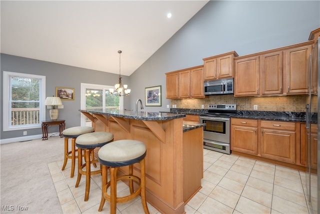 kitchen featuring a center island with sink, hanging light fixtures, dark stone countertops, stainless steel appliances, and a chandelier