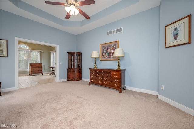 interior space featuring a raised ceiling, ceiling fan, and light colored carpet