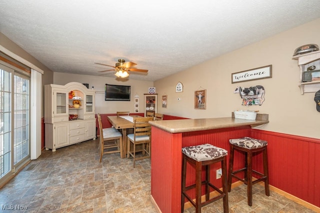 kitchen featuring ceiling fan, a kitchen bar, a textured ceiling, and kitchen peninsula