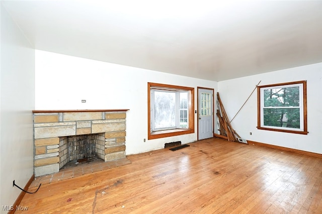 unfurnished living room with a stone fireplace, a wealth of natural light, and hardwood / wood-style flooring