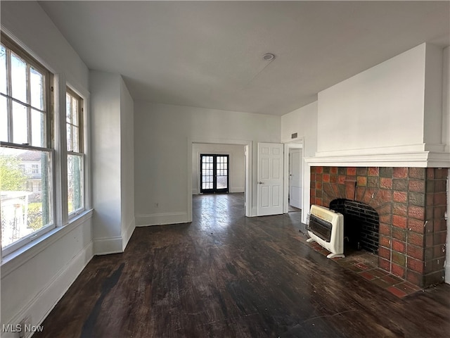 unfurnished living room featuring dark hardwood / wood-style flooring, heating unit, a brick fireplace, and plenty of natural light