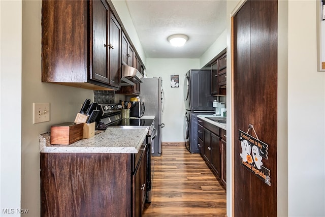 kitchen with stacked washing maching and dryer, hardwood / wood-style floors, stainless steel appliances, and dark brown cabinets