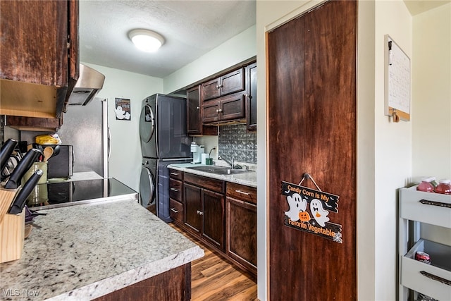 kitchen featuring sink, stacked washer / dryer, exhaust hood, dark brown cabinets, and light wood-type flooring