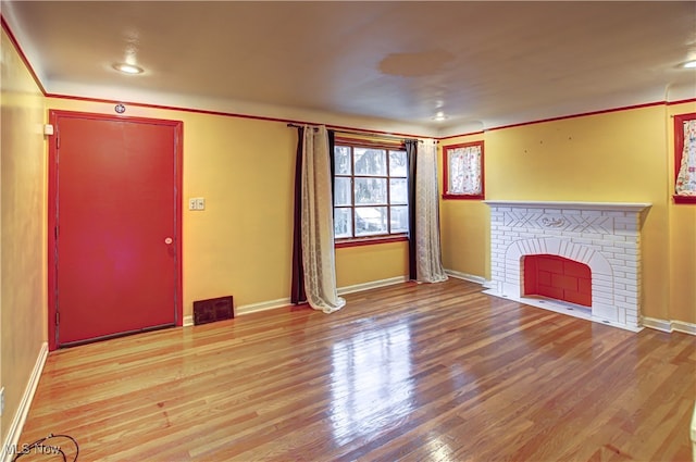 unfurnished living room with a brick fireplace, light hardwood / wood-style flooring, and ornamental molding