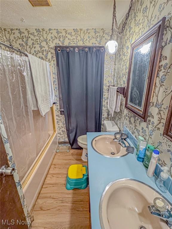 1330 W 18th St, Lorain, OH 44052 - full bath with wallpapered walls, wood finished floors, a textured ceiling, toilet, and shower / tub combo with curtain