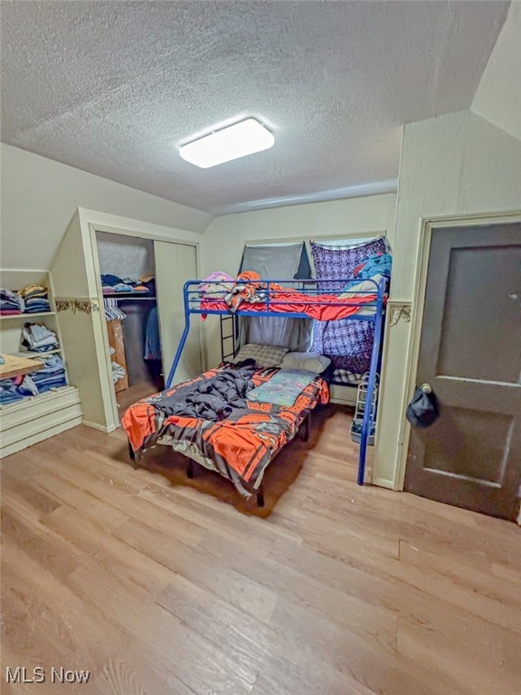 bedroom with wood-type flooring, a textured ceiling, a closet, and lofted ceiling