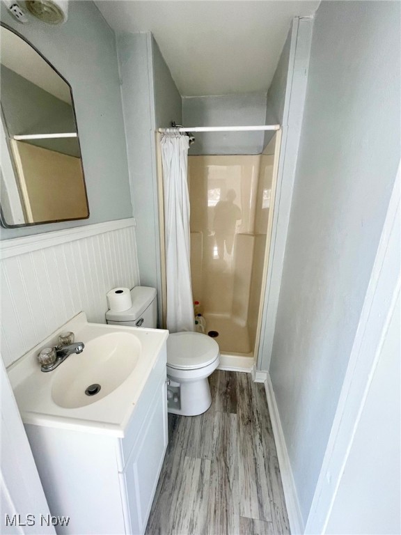 bathroom with hardwood / wood-style floors, curtained shower, vanity, and toilet