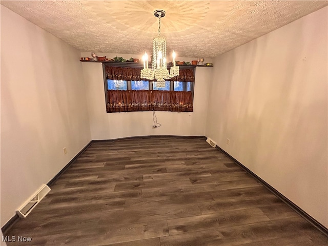 unfurnished dining area with a textured ceiling, an inviting chandelier, and dark wood-type flooring