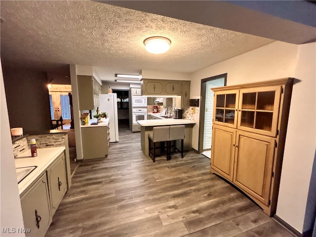 kitchen with decorative backsplash, dark hardwood / wood-style flooring, white appliances, a breakfast bar area, and a textured ceiling