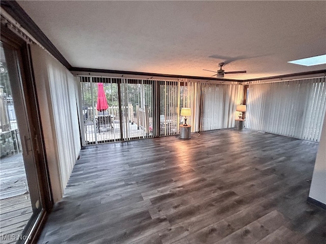 unfurnished living room featuring a skylight, ceiling fan, dark wood-type flooring, crown molding, and a textured ceiling