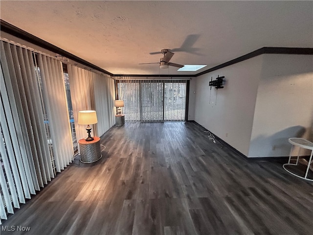 unfurnished living room featuring a skylight, ceiling fan, dark hardwood / wood-style floors, and ornamental molding