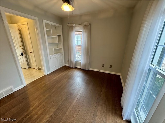 empty room with built in shelves and wood-type flooring