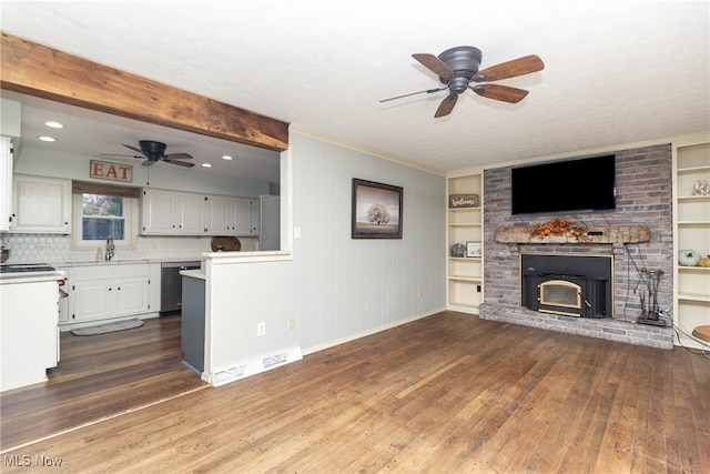 unfurnished living room featuring built in shelves, beam ceiling, dark hardwood / wood-style flooring, a brick fireplace, and ceiling fan