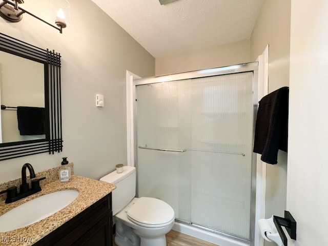 bathroom featuring a textured ceiling, wood-type flooring, vanity, an enclosed shower, and toilet