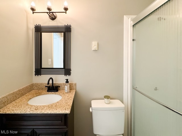 bathroom featuring a shower with door, vanity, and toilet