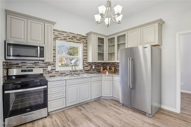 kitchen featuring stainless steel appliances, light wood-type flooring, backsplash, light stone countertops, and sink