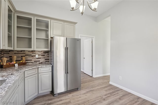 kitchen featuring stainless steel refrigerator, light stone countertops, a chandelier, light hardwood / wood-style flooring, and decorative backsplash