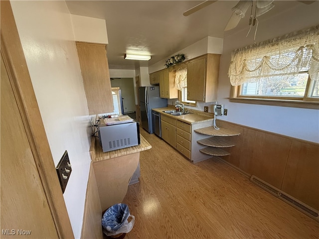 kitchen with light hardwood / wood-style floors, sink, appliances with stainless steel finishes, ceiling fan, and wooden walls