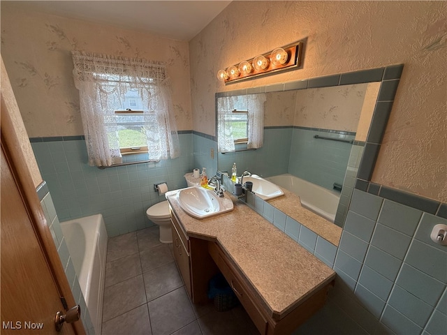 bathroom featuring tile patterned flooring, vanity, a bath, toilet, and tile walls