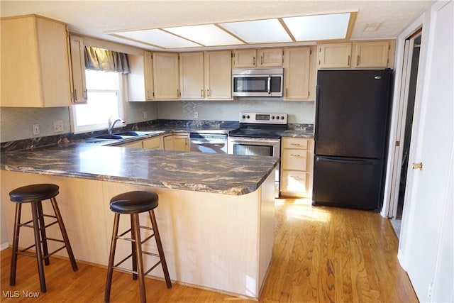 kitchen with appliances with stainless steel finishes, a breakfast bar, sink, kitchen peninsula, and light hardwood / wood-style flooring