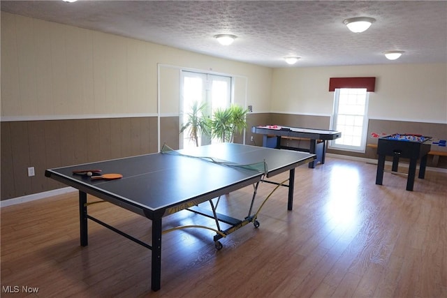 recreation room with a wealth of natural light, wooden walls, hardwood / wood-style floors, and a textured ceiling