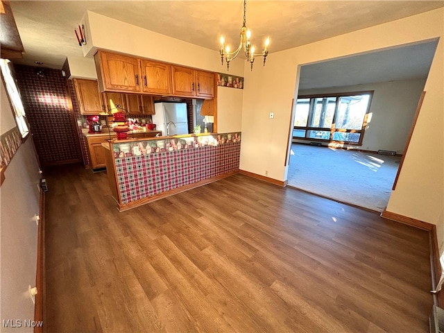 kitchen featuring kitchen peninsula, a notable chandelier, dark hardwood / wood-style floors, pendant lighting, and stainless steel fridge