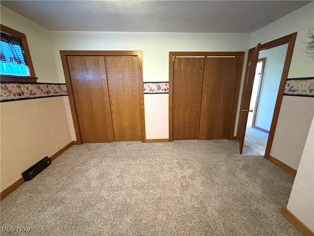 unfurnished bedroom featuring light carpet and two closets