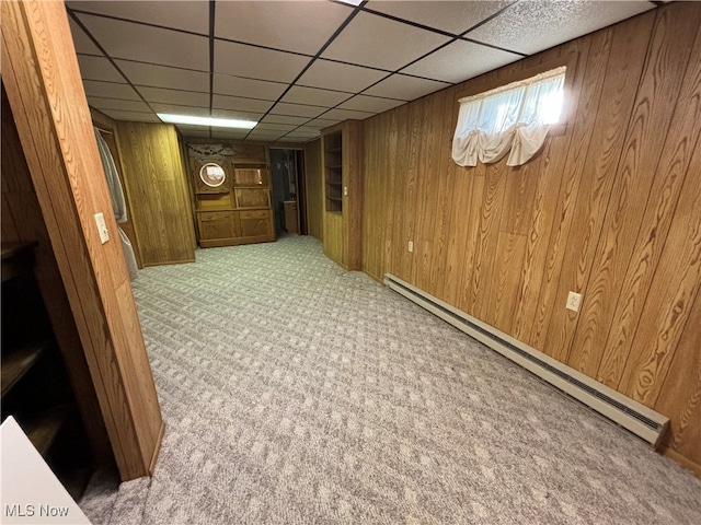 basement featuring wood walls, a paneled ceiling, light carpet, and a baseboard heating unit