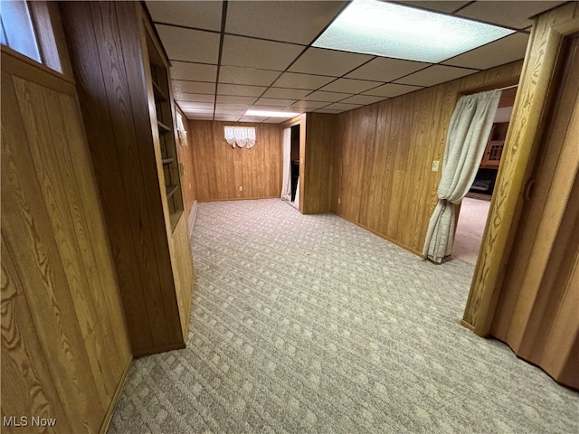 basement with wood walls, a paneled ceiling, and light carpet