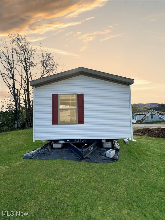 back house at dusk featuring a lawn