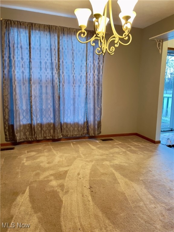 carpeted empty room with an inviting chandelier