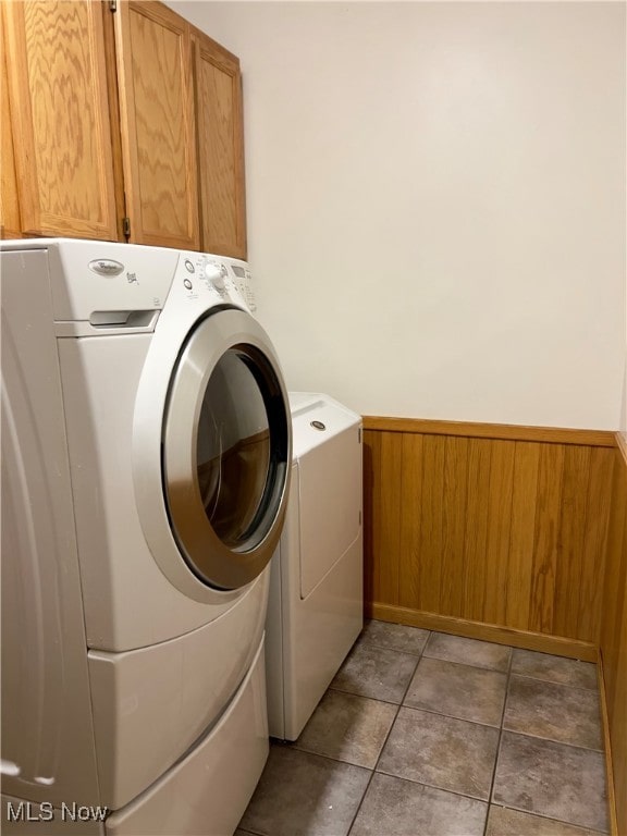 laundry area featuring tile patterned flooring, wooden walls, cabinets, and washing machine and clothes dryer