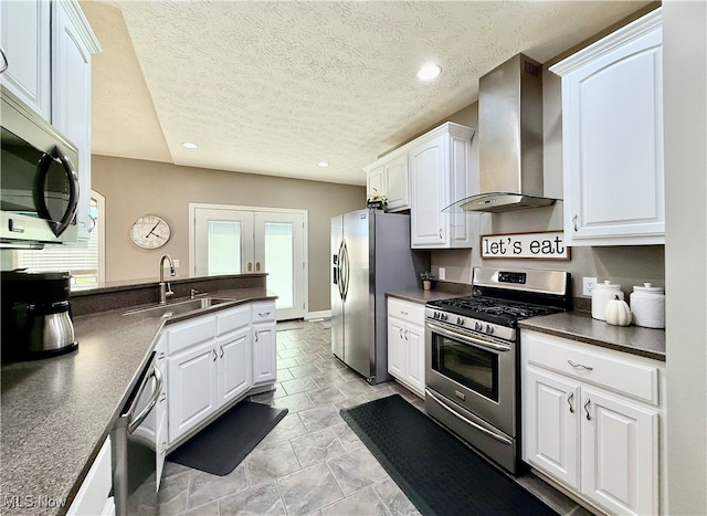 kitchen with sink, wall chimney exhaust hood, a textured ceiling, appliances with stainless steel finishes, and white cabinetry