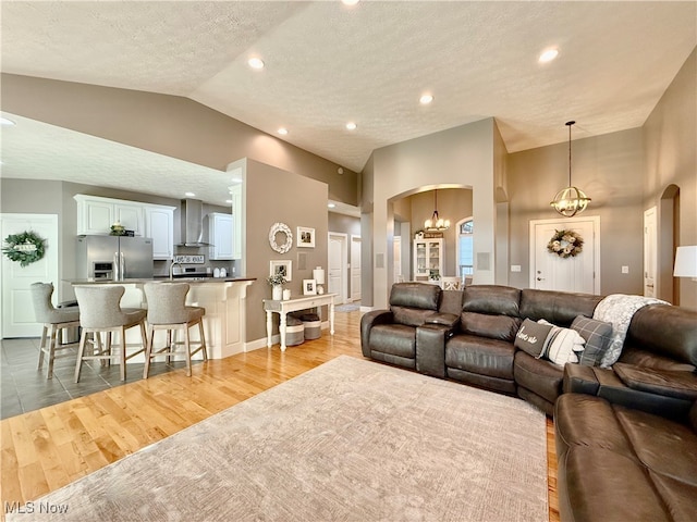 living room with high vaulted ceiling, sink, light hardwood / wood-style flooring, a textured ceiling, and a chandelier