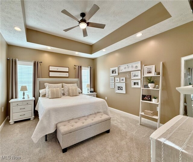 carpeted bedroom featuring multiple windows, a textured ceiling, a raised ceiling, and ceiling fan