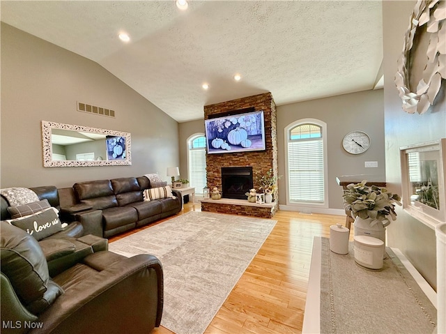 living room featuring hardwood / wood-style flooring, a stone fireplace, lofted ceiling, and a textured ceiling