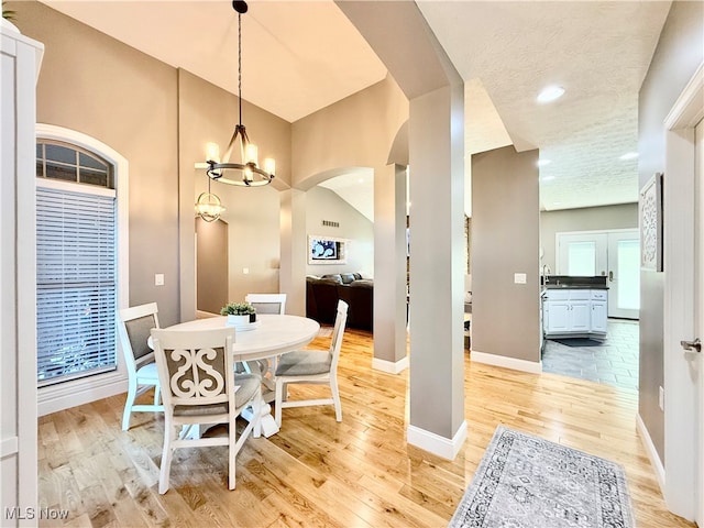 dining room with a textured ceiling, light hardwood / wood-style floors, vaulted ceiling, and a notable chandelier