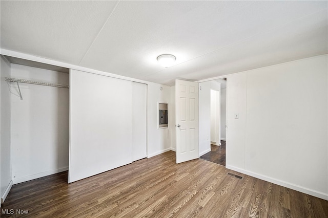 unfurnished bedroom with dark wood-type flooring, electric panel, a textured ceiling, and a closet