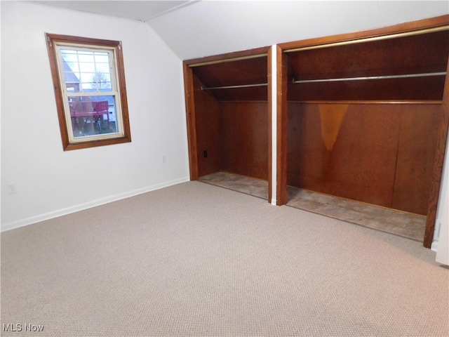 unfurnished bedroom with two closets, light colored carpet, and vaulted ceiling