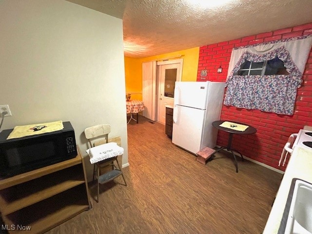 kitchen with a textured ceiling, stove, hardwood / wood-style flooring, white fridge, and brick wall