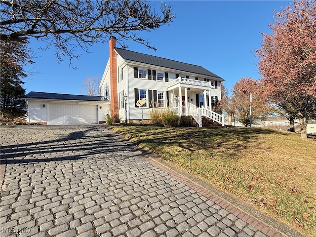 colonial inspired home featuring a garage, an outdoor structure, a front lawn, and a balcony