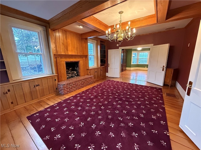 unfurnished living room featuring a fireplace, beamed ceiling, wood-type flooring, and plenty of natural light