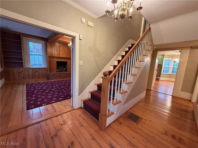 staircase with hardwood / wood-style floors, a fireplace, a chandelier, and crown molding